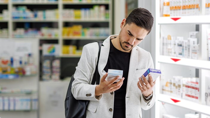 A man compares over-the-counter medication at a pharmacy. If you have constipation, magnesium supplements can help to relieve it.
