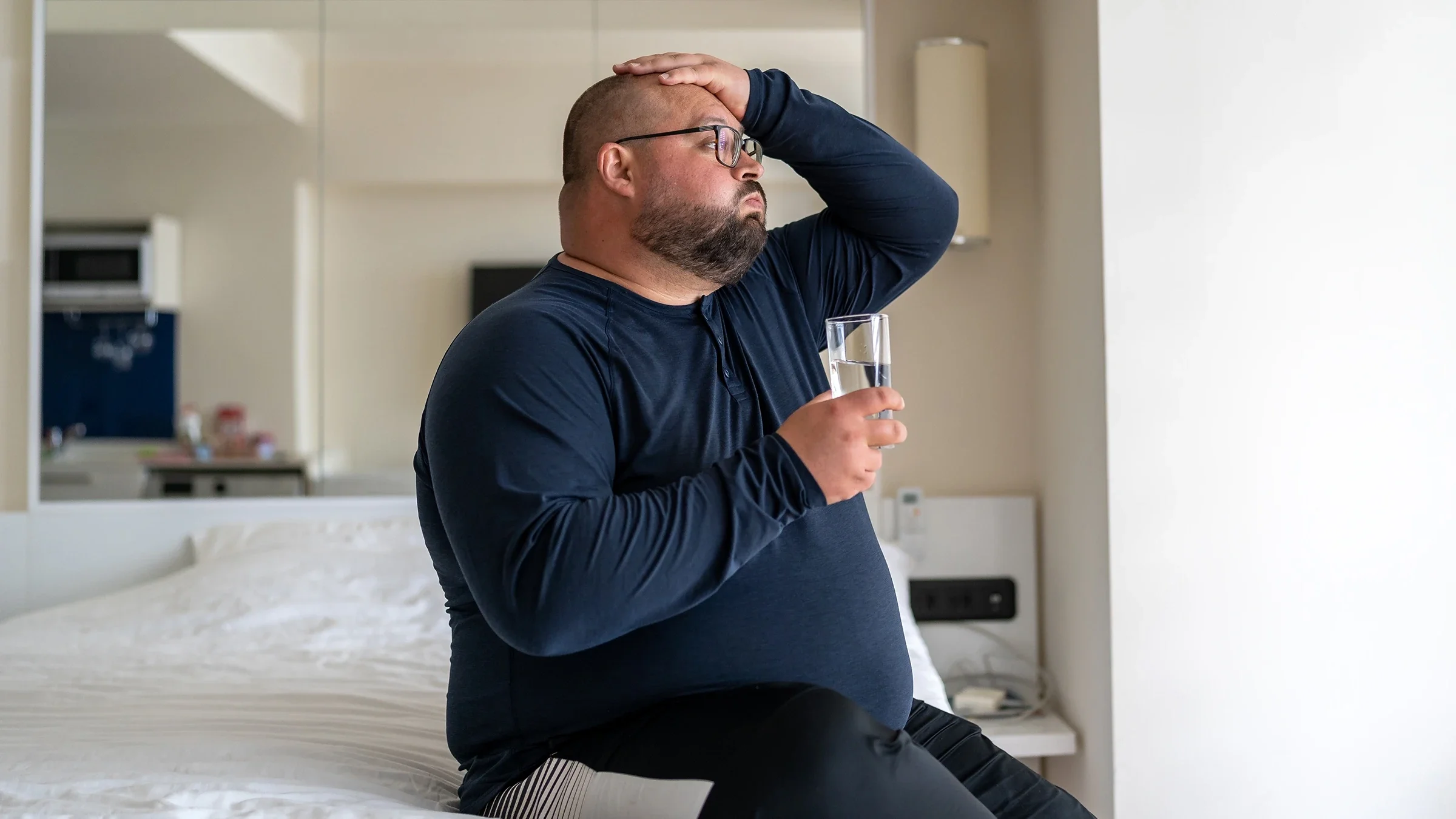 A man in bed drinks a glass of water. Hydration and rest can help you get over a cold quicker.