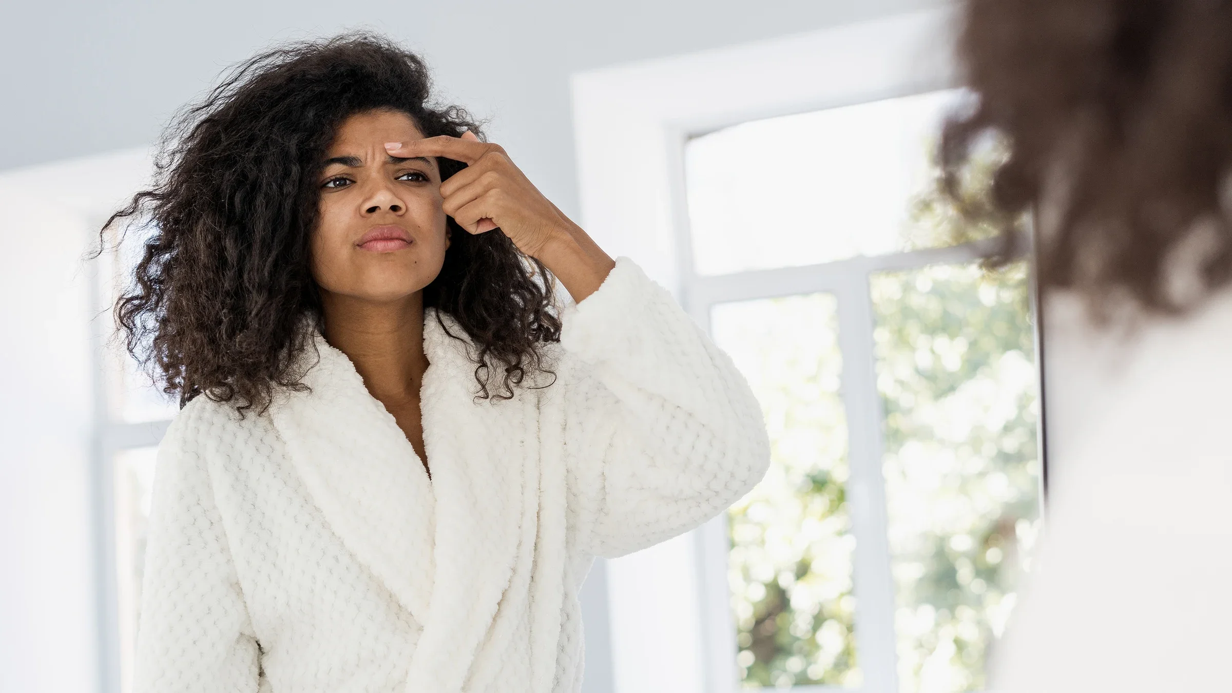 Woman looking in the mirror at her skin.
brizmaker/iStock via Getty Images