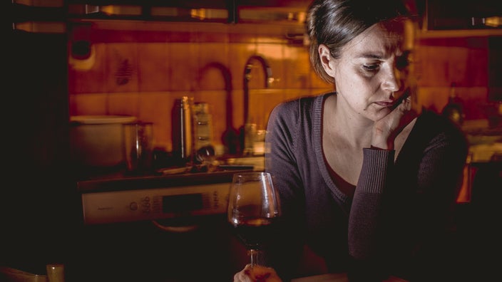 A person looking sad with a half-empty glass of wine.