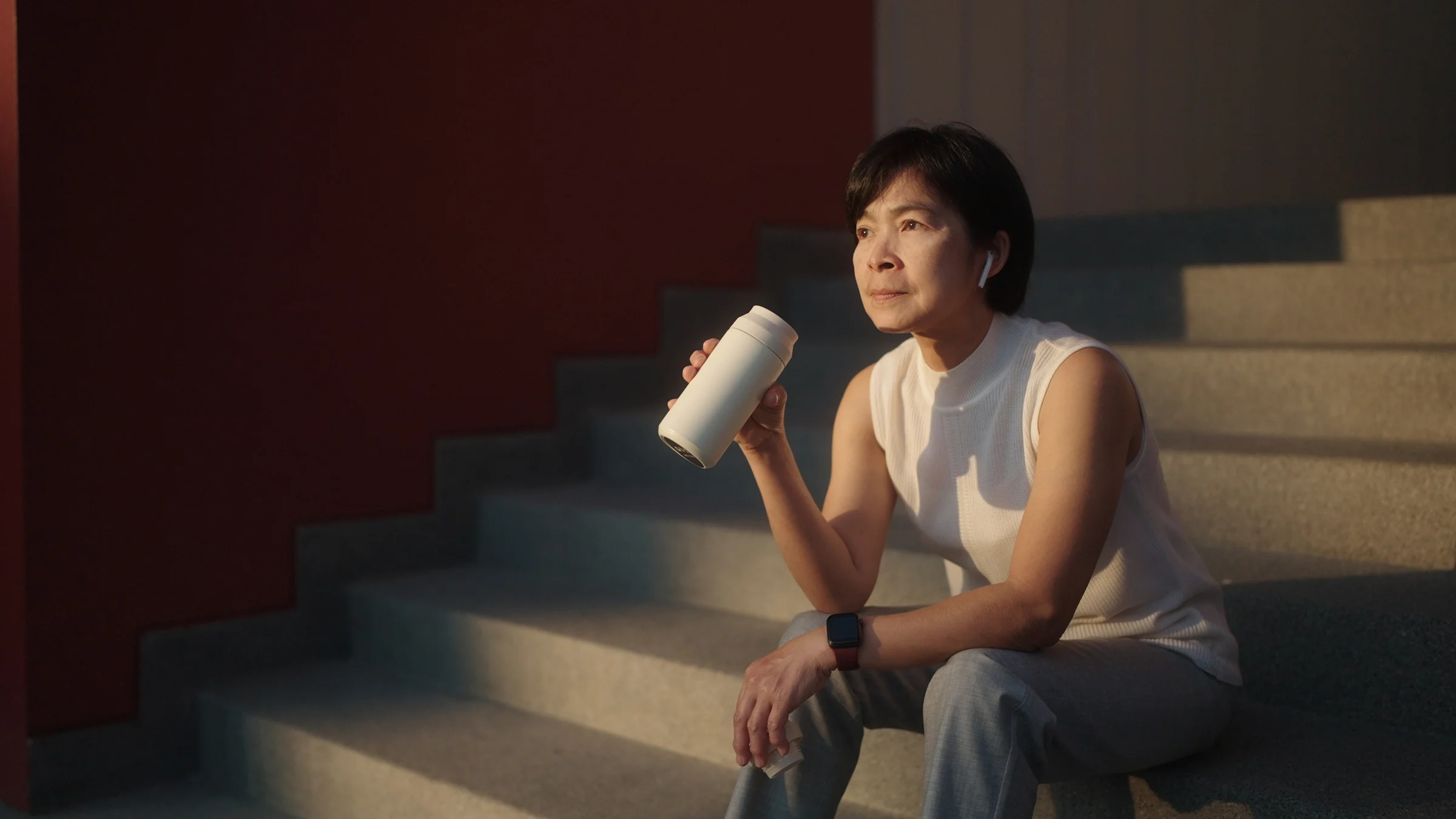 A woman wearing a smartwatch drinks water while taking a break. 