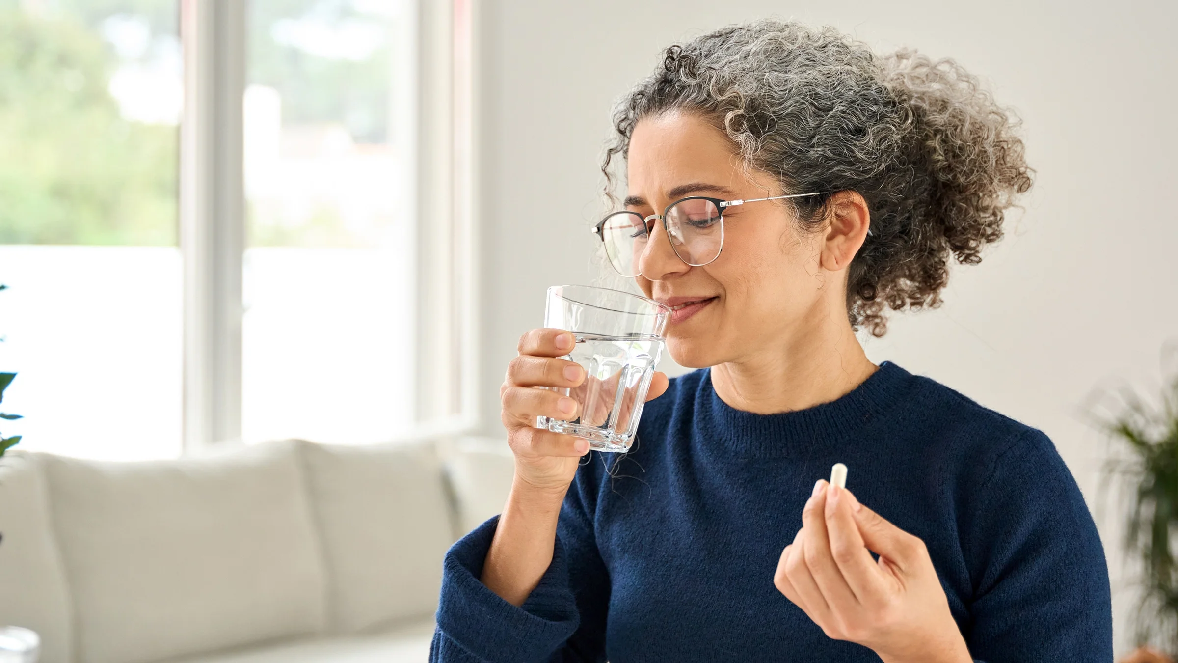 A woman is taking a pill with a glass of water.