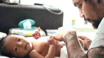 Parenthood: Diaper rash treatment: tattooed dad changing diaper 837671344