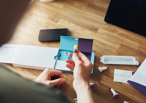 Close-up of a man opening an at home blood test kit, he is holding a small test tube in his hand.
SouthWorks/iStock via Getty Images