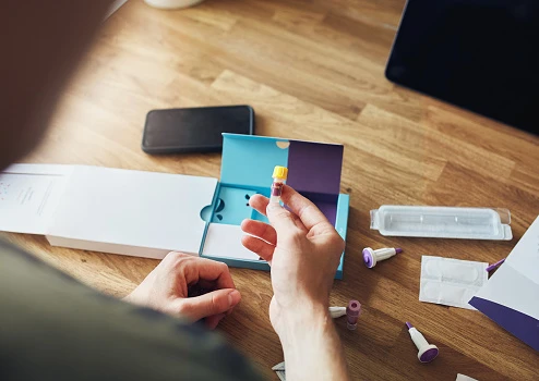 Close-up of a man opening an at home blood test kit, he is holding a small test tube in his hand.