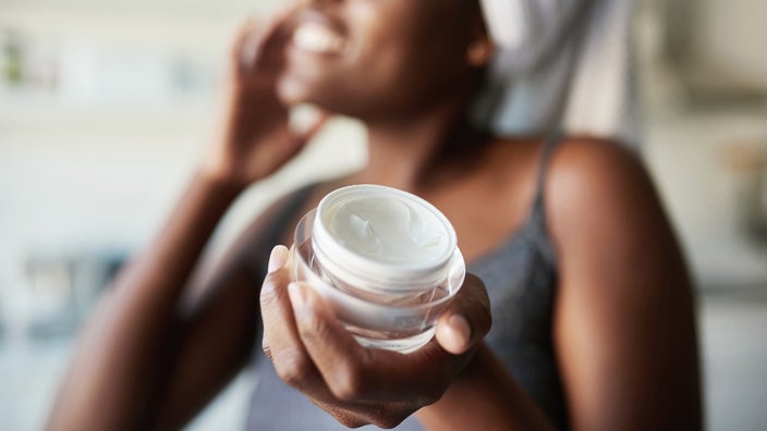 Close-up on a woman using face cream. The focus is on her hand and the jar of cream.