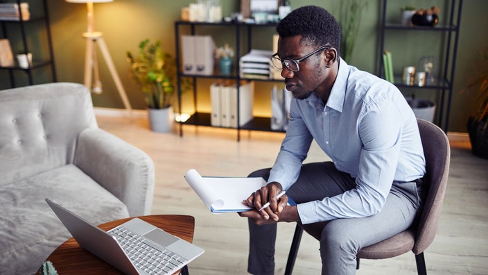 A counselor takes notes during an online therapy session.