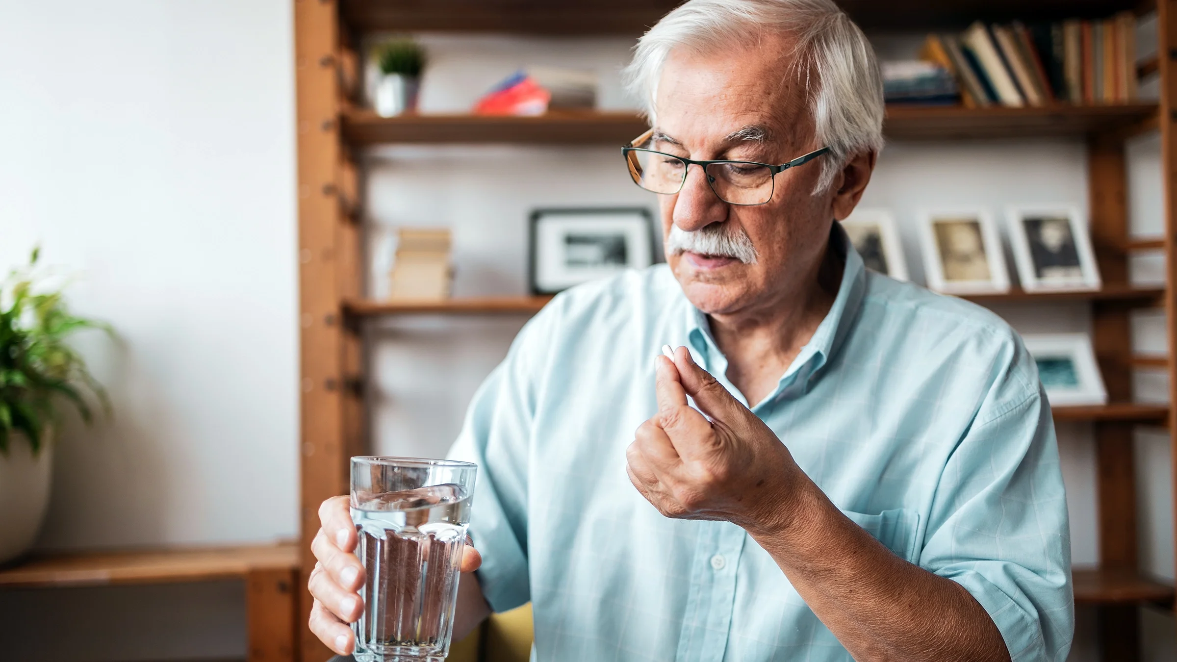 Senior man holding a glass of water and taking his pill.