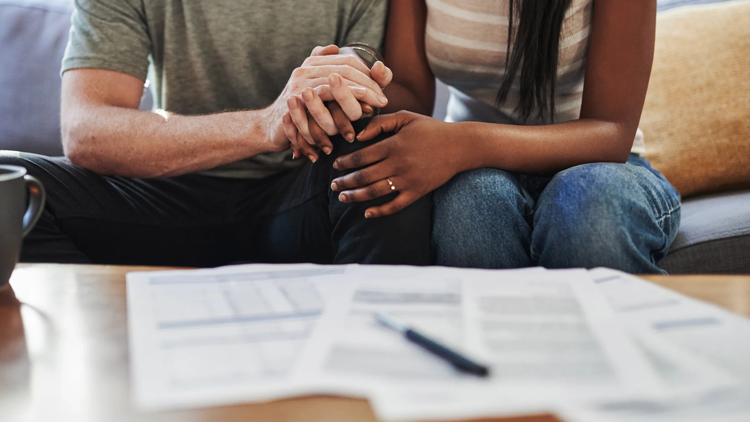 Cropped shot of a couple holding hands and looking down at paperwork on the coffee table in front of them.
mapodile/E+ via Getty Images