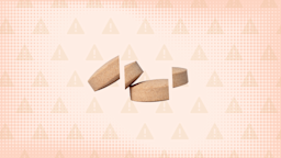 In the center of a light orange background with texture and warning sign pattern are two tan-orange pills cut into thirds.
GoodRx Health