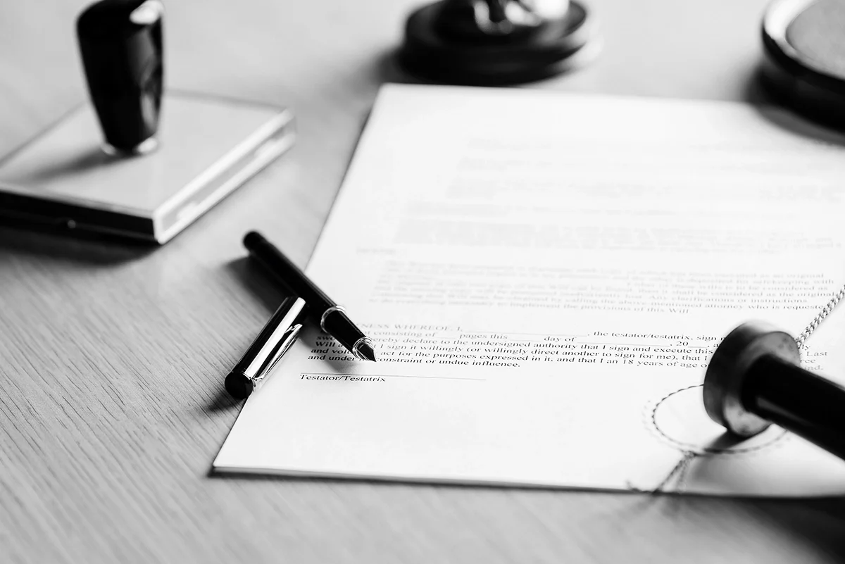 Black and white image of legal paperwork on a table with an open pen and rubber stamps surrounding it.