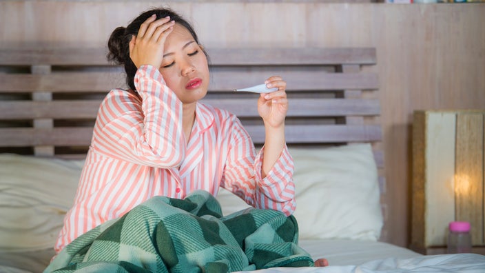 A person with a fever checking their thermometer.