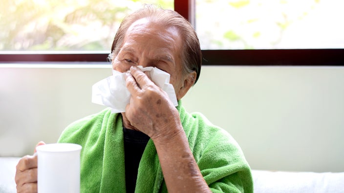 Older man blowing his nose while drinking tea.