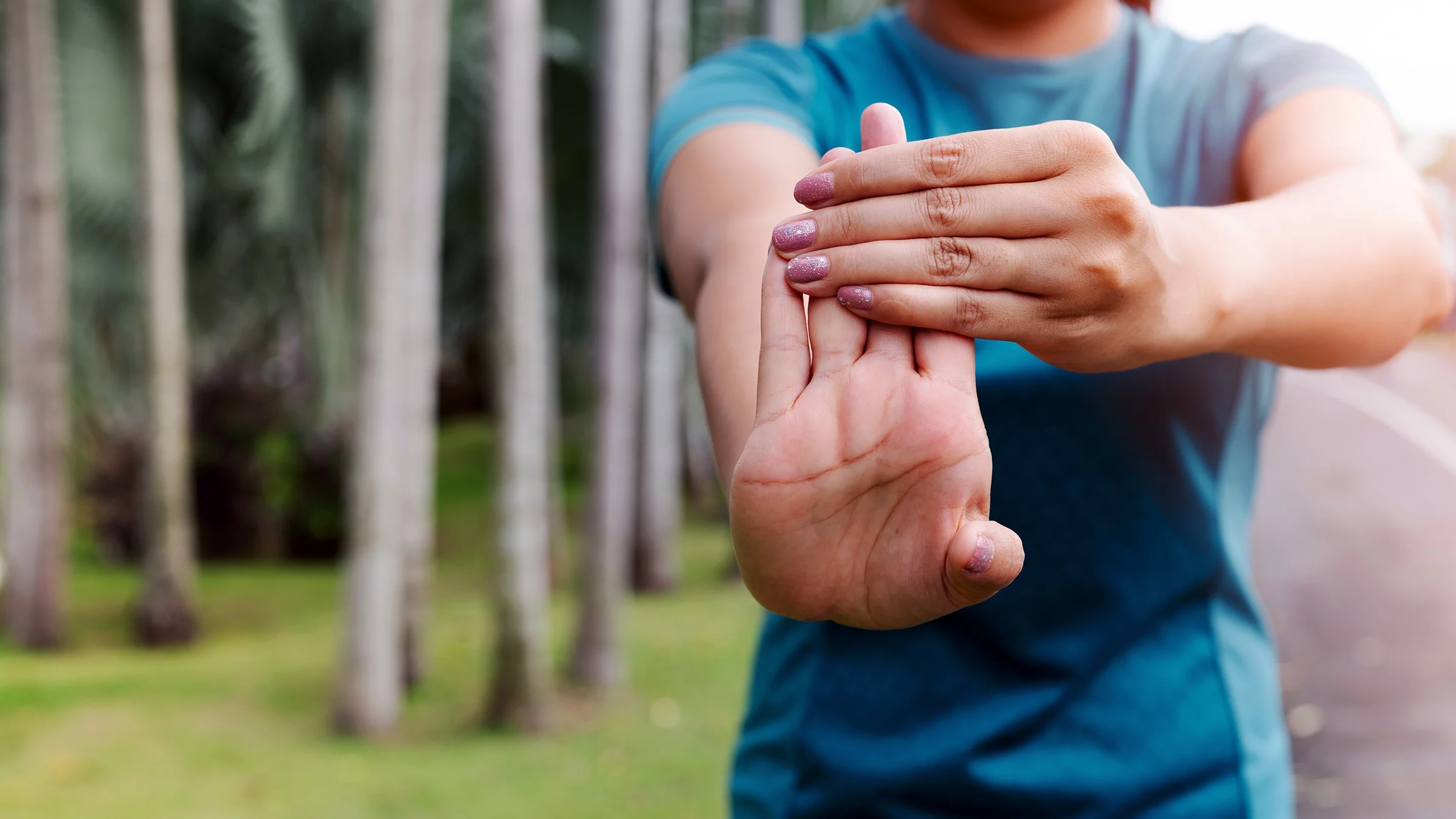 A woman stretches her forearm outdoors.