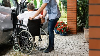 Health: Medicare: man assists woman in wheelchair into car 1082955788