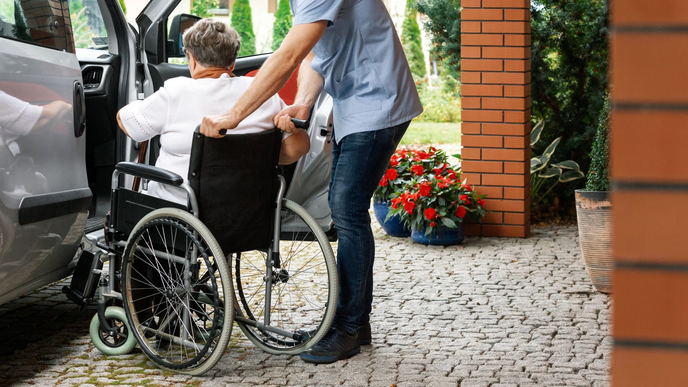 A man helps a woman in a wheelchair get into a car.