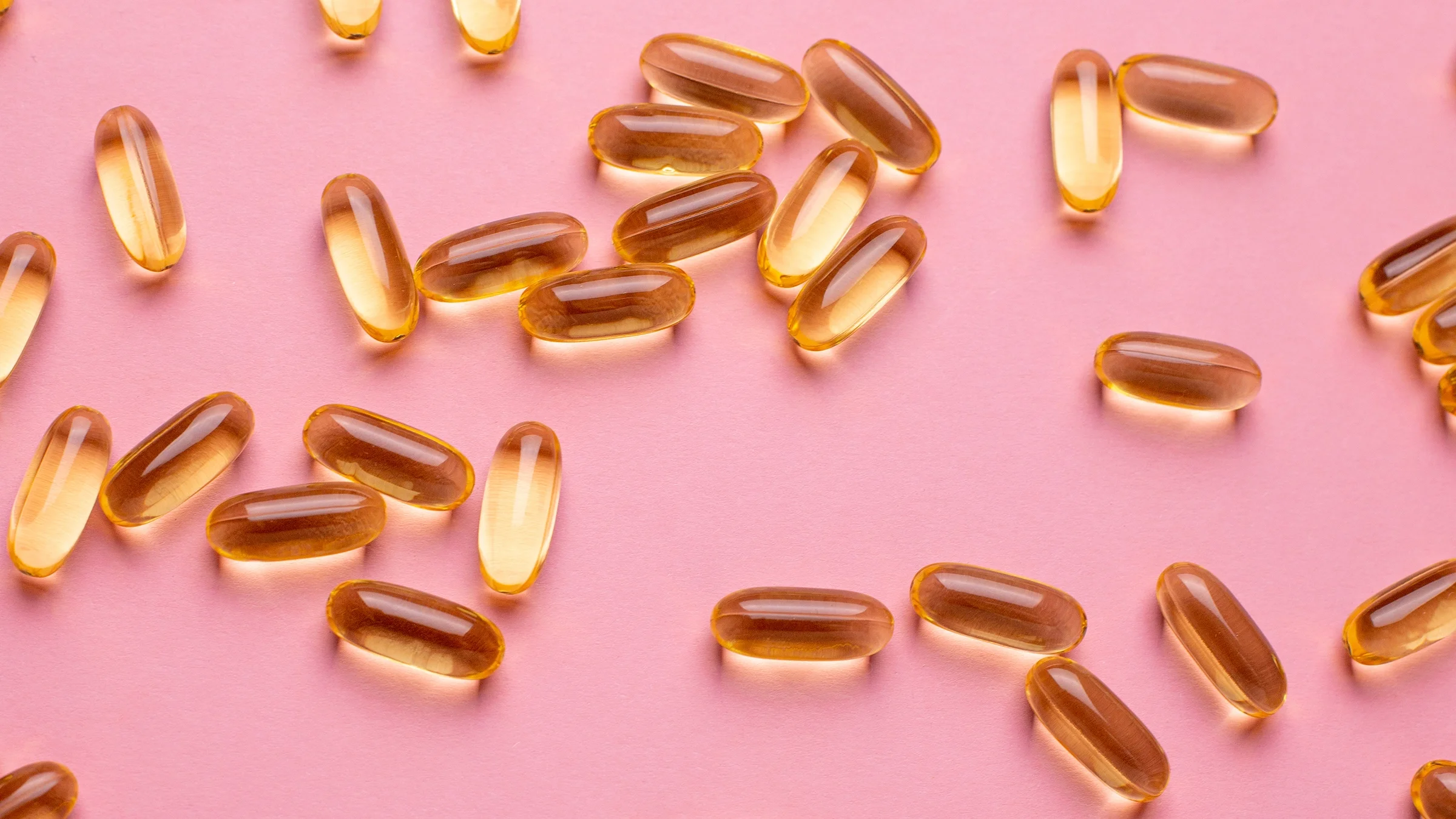 There are scattered vitamin D pills on a light pink background.