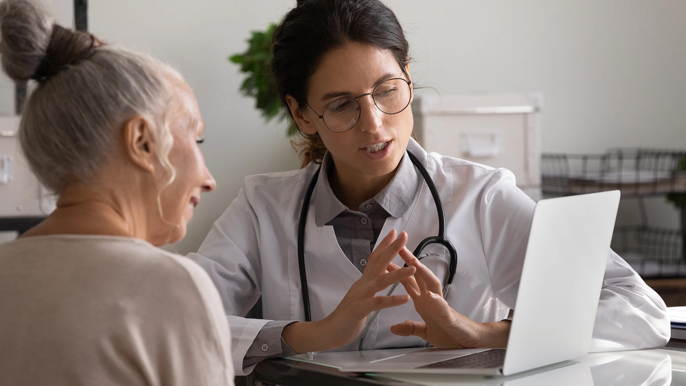 A doctor reviews results on a laptop with an older adult.