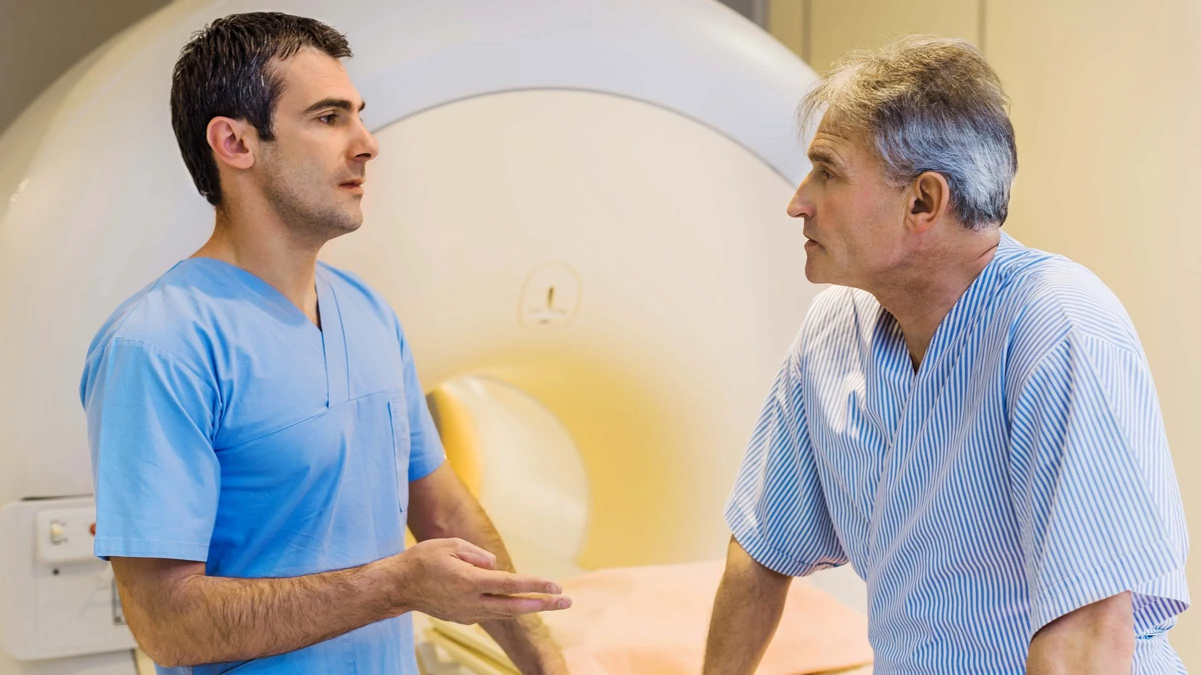 Older man with gray hair talking to the radiologist in the MRI room before his scan.