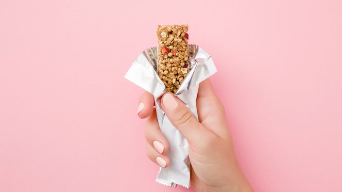 Hand holding granola bar on pink background