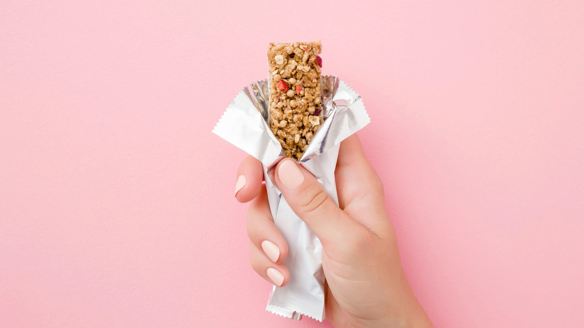 Hand holding granola bar on pink background