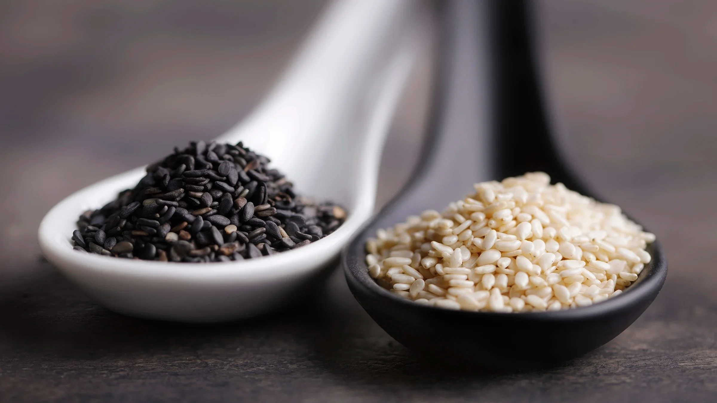 Spoonfuls of black and white sesame seeds lie on a table.