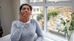 A woman suffering from daytime sleepiness yawns and covers her mouth.
SolStock/E+ via Getty Images
