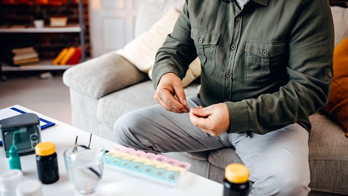 A man is organizing his medication in a pill dispenser.