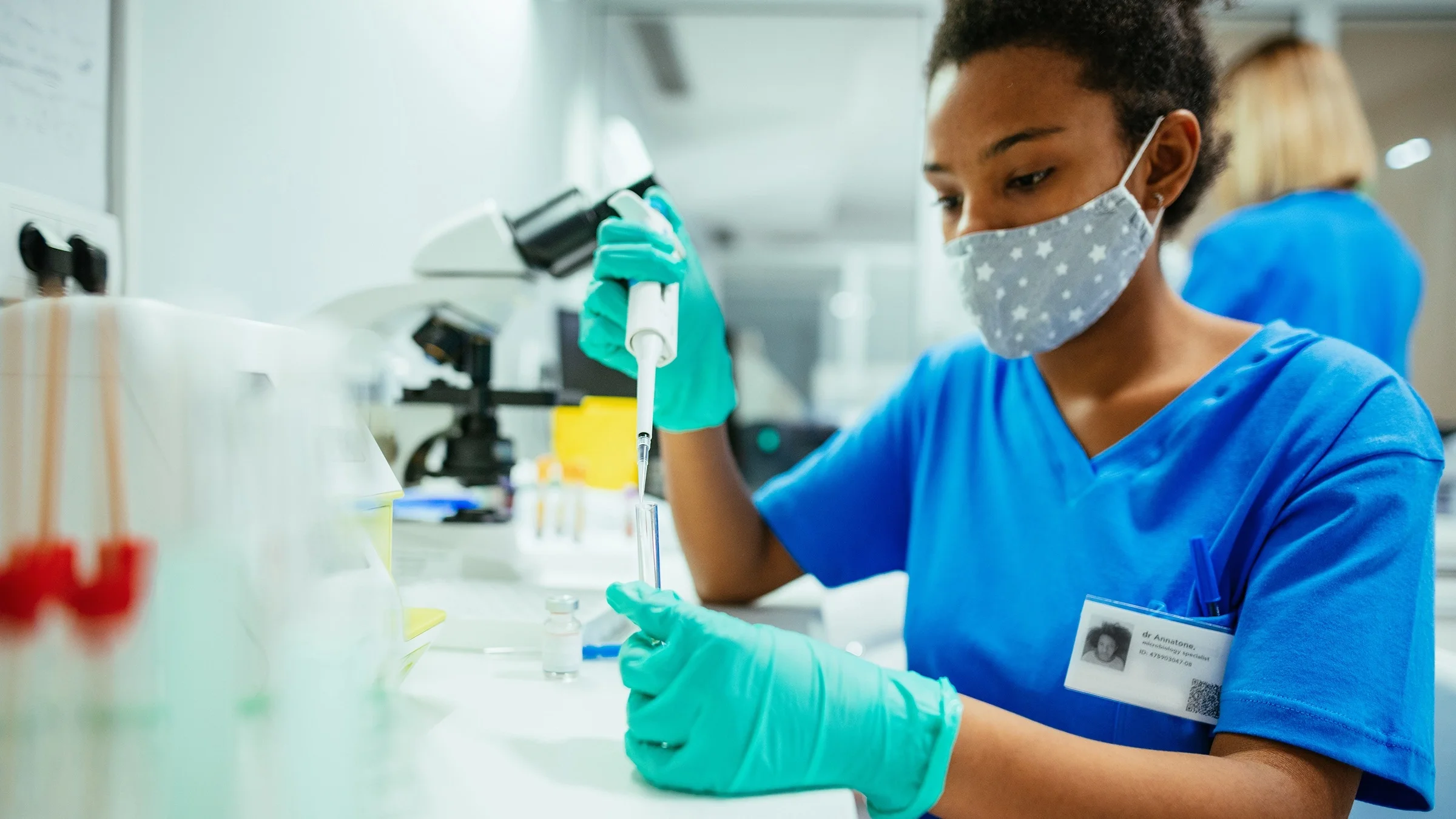 Doctor in the lab with syringes and test tubes wearing a cloth mask with stars on it.