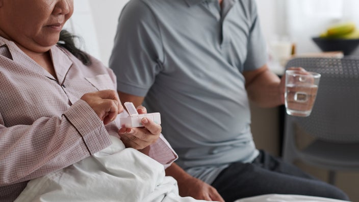 A person taking medicine is being offered water by their spouse.