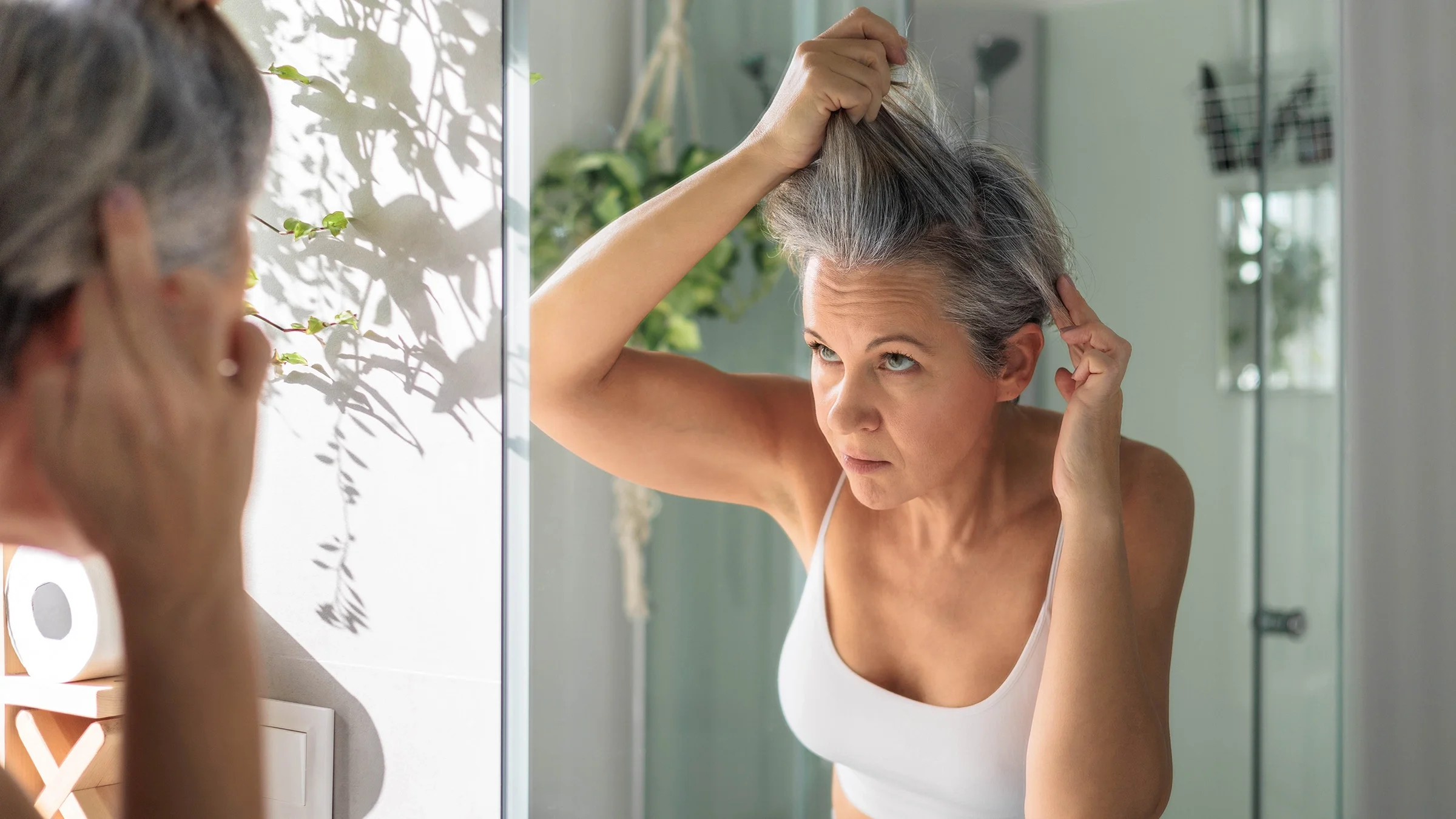 Woman examining her hair in a mirror.