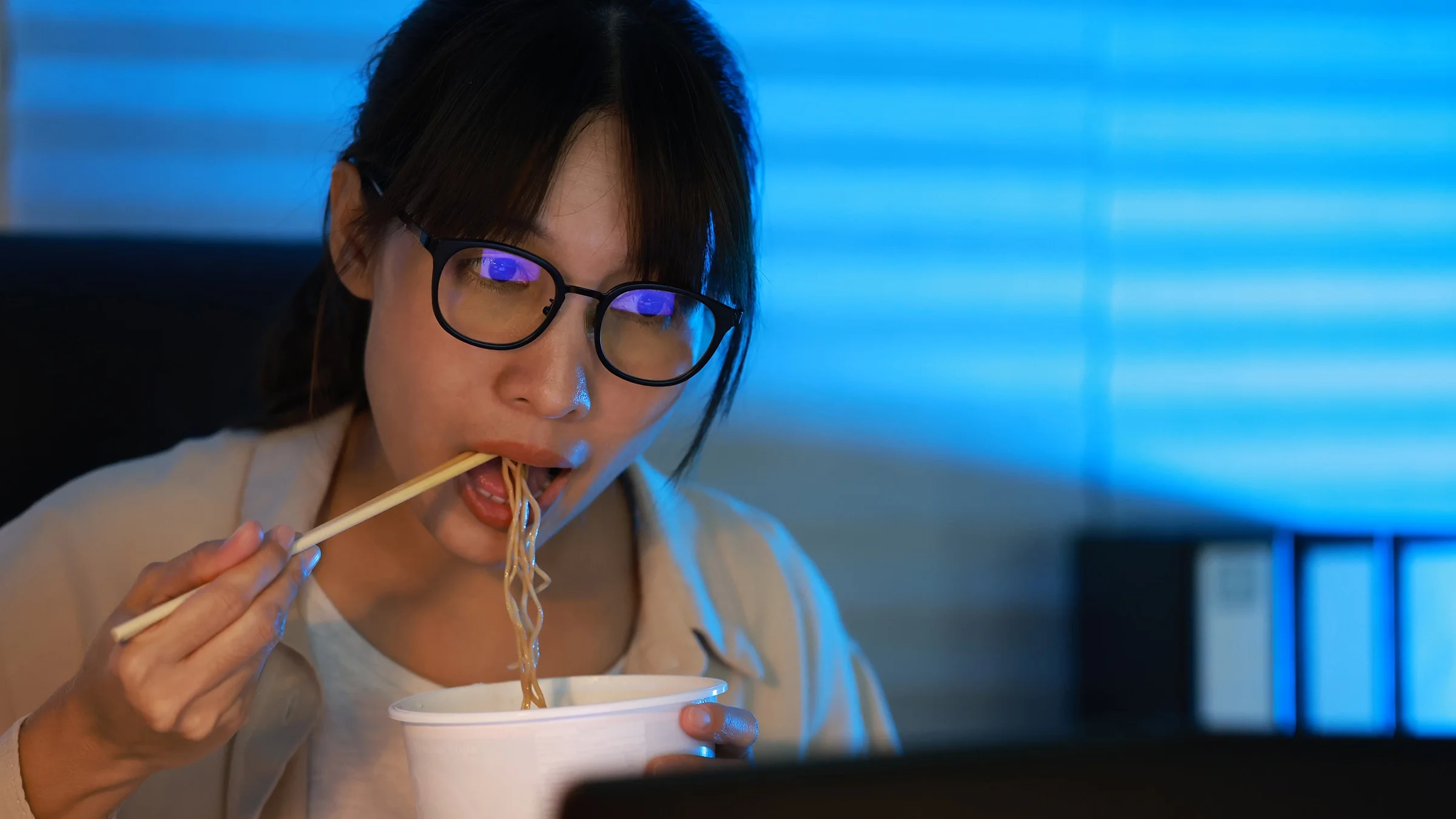 Woman eats instant ramen while working on a laptop