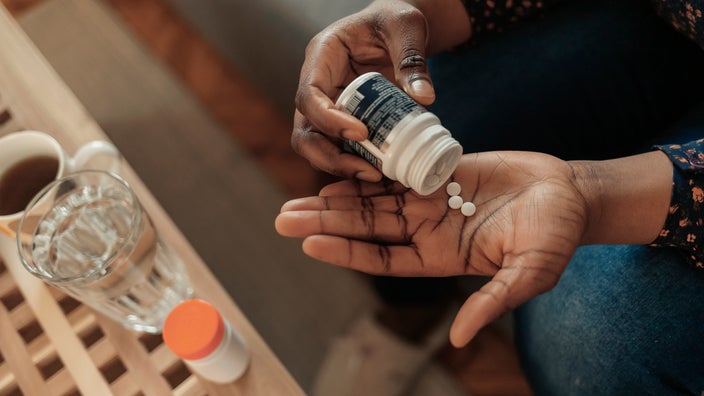 Cropped overhead shot of a woman pouring pills into her hand from a pill bottle.