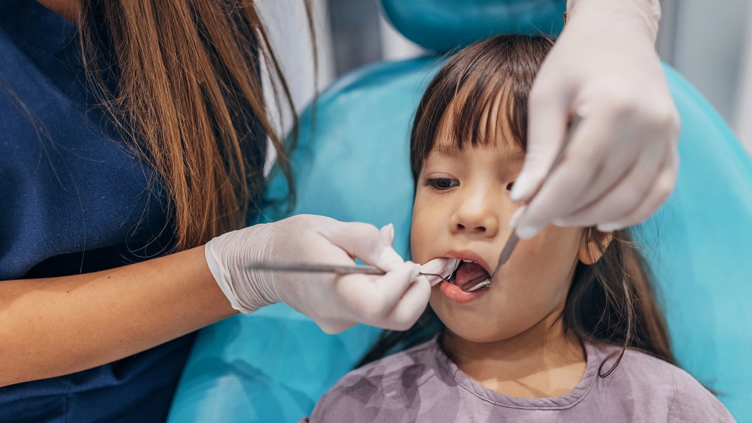 A dentist examines a child’s teeth. Not brushing and flossing your teeth properly and teeth grinding are some of the causes of cavities. 