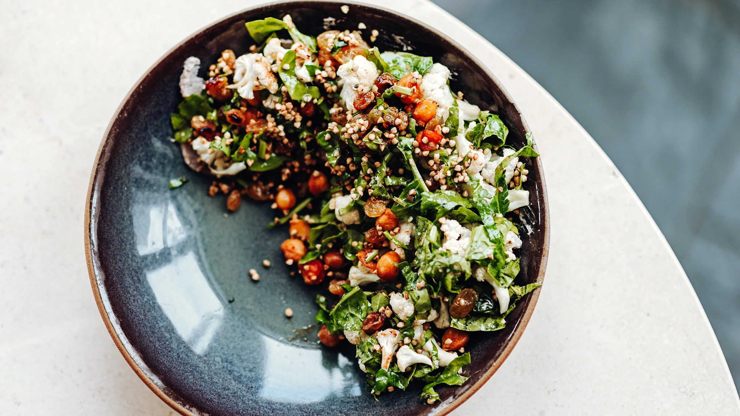 Overhead shot photo of a healthy cauliflower, spinach, quinoa bowl on a white quartz table.