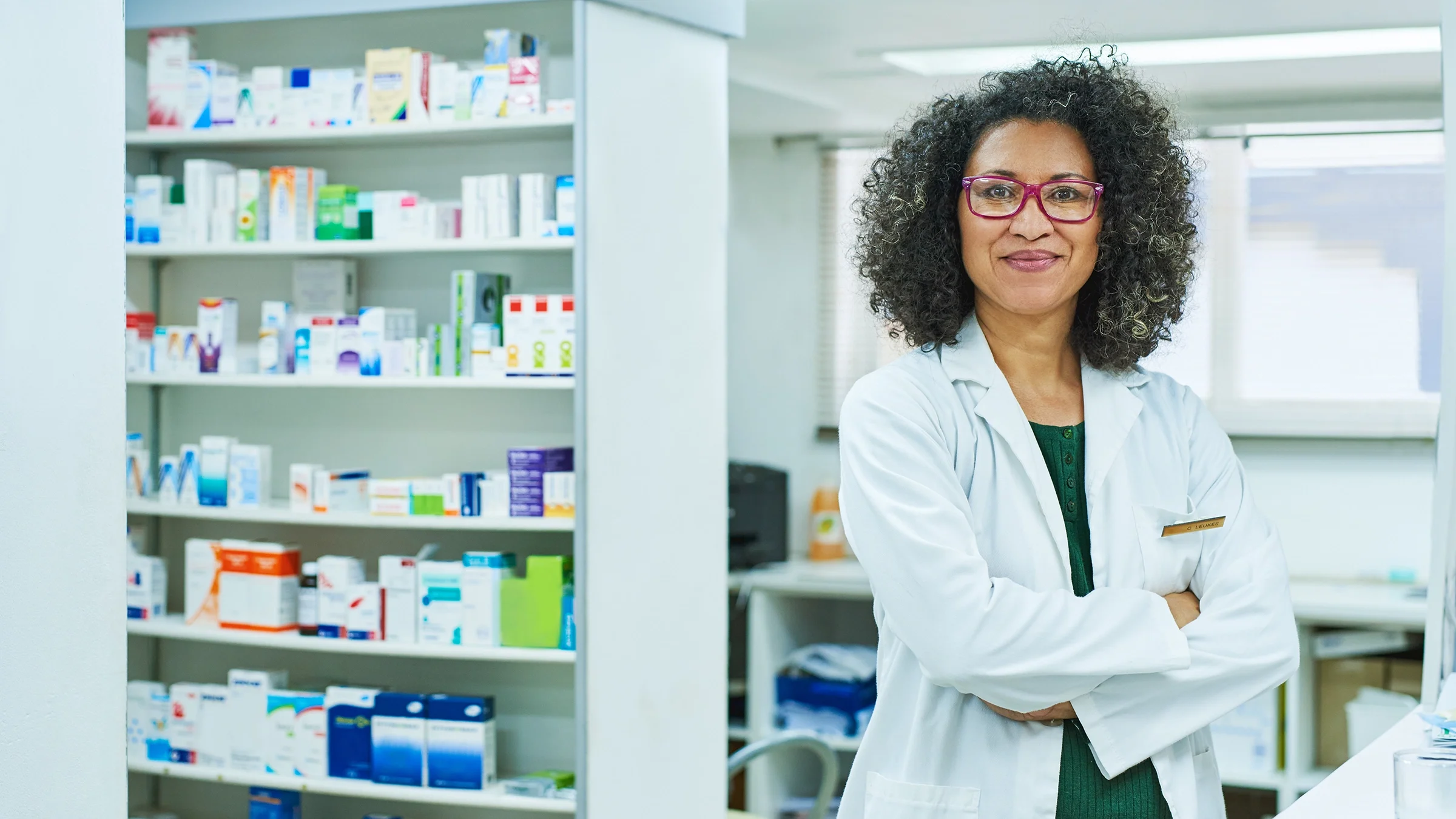 Portrait of a pharmacist in the back of the pharmacy. She has her arms crossed in front of her chest.