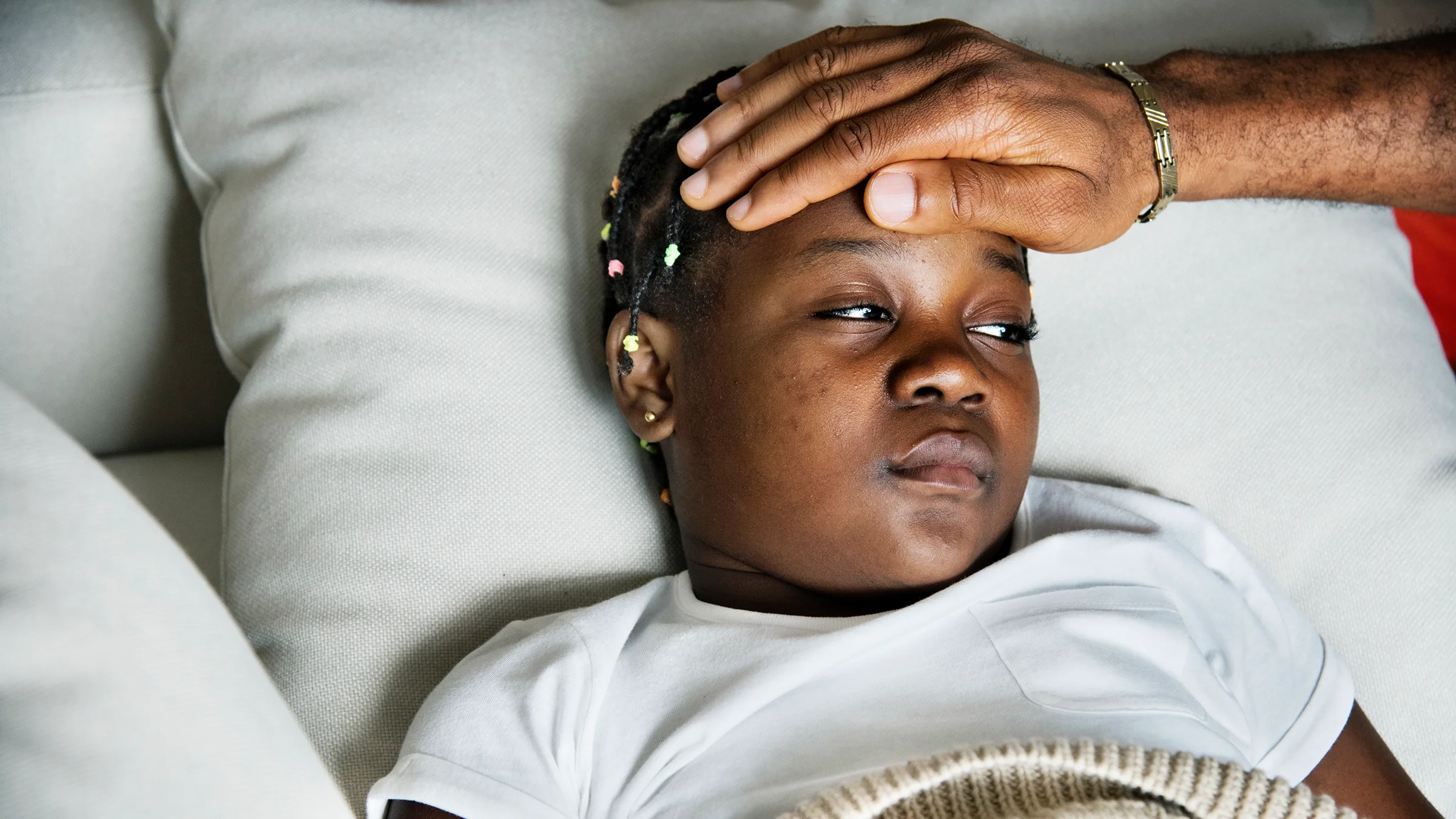 Young child sick in bed as a parent uses their hand to test the child’s temperature.