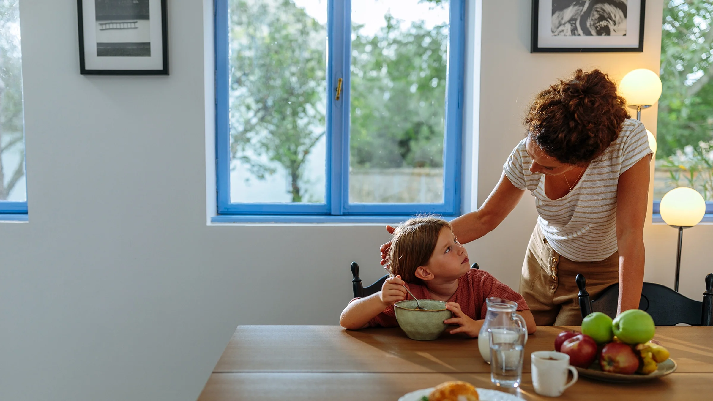A woman talks to her daughter, who’s eating breakfast.