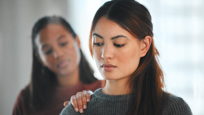 A woman has her hand on her friend’s shoulder comforting her.