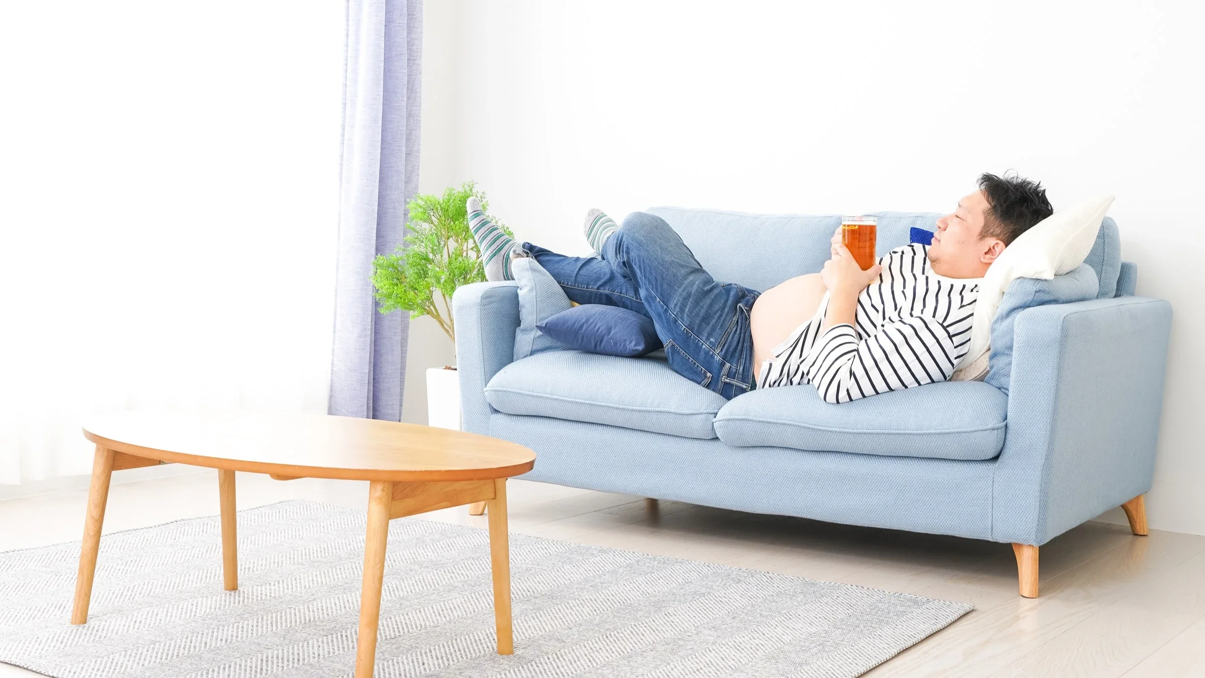 A peeson with a beer belly drinking on their couch.