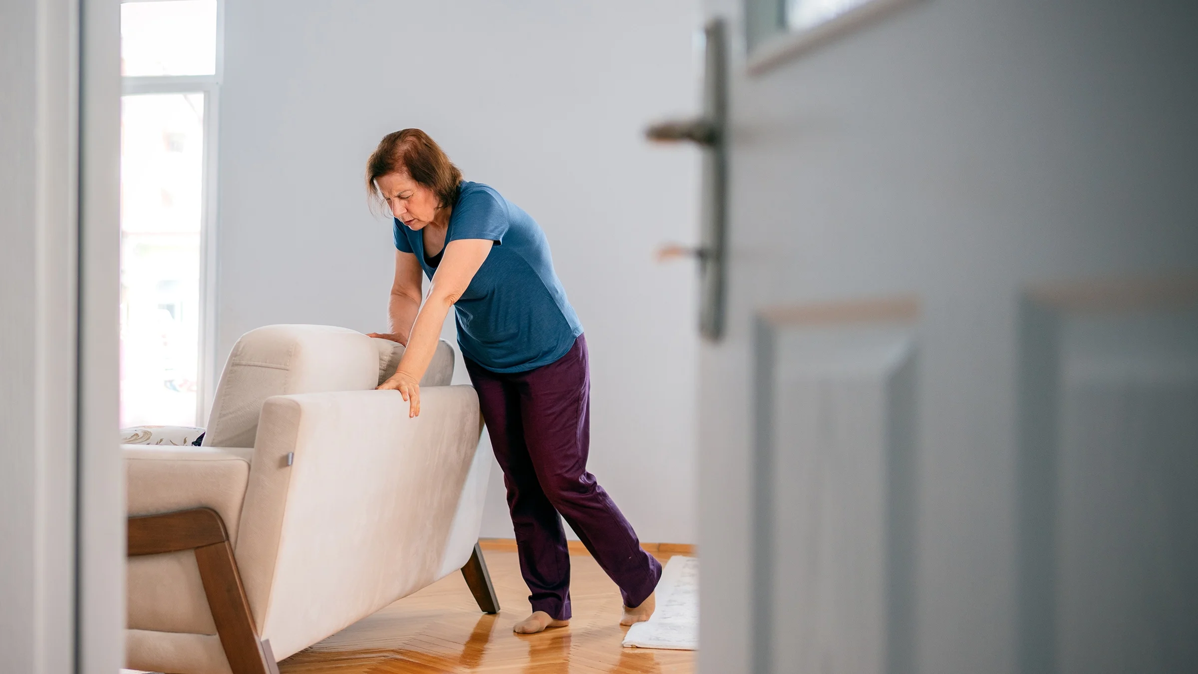 Older woman bracing herself with the back of the couch because she is dizzy from vertigo.
