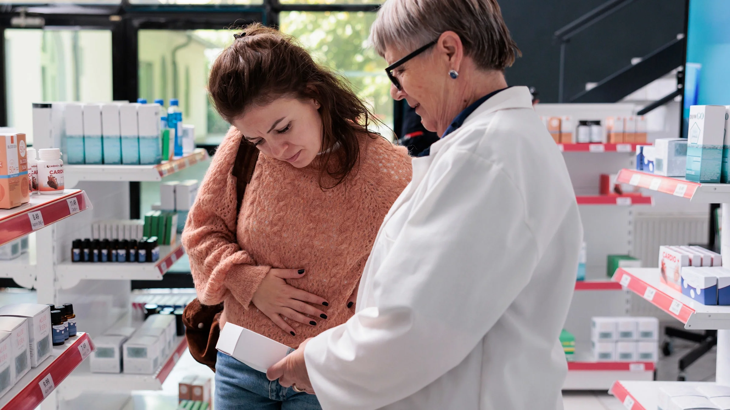A customer with stomach pain talking to a pharmacist about medication options.