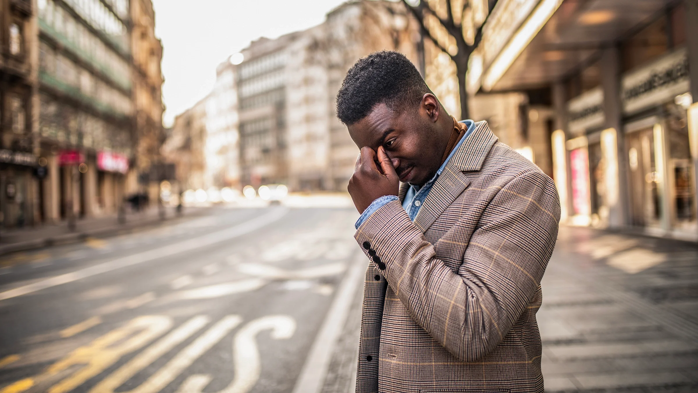 Man standing on the street holding his head in his hand. He looks like he has a severe headache.