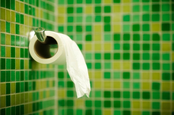 A roll of toilet paper hanging in a bathroom with green and yellow tiles.