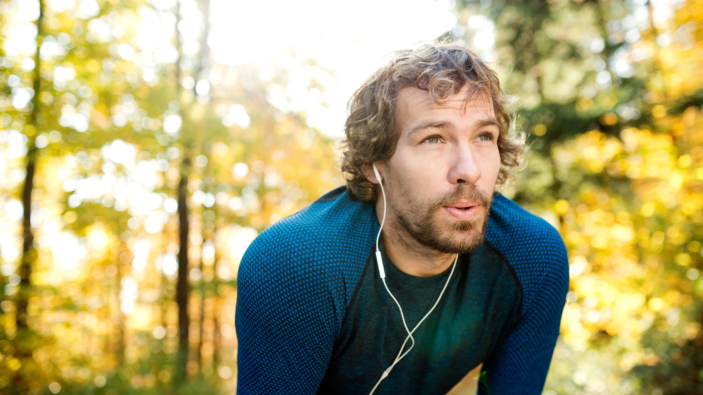 A man wearing headphones takes a break during a run outside.
