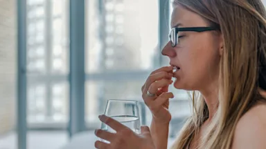 The side profile of someone holding a glass of water and taking a pill. 
ljubaphoto/E+ via Getty Images 
