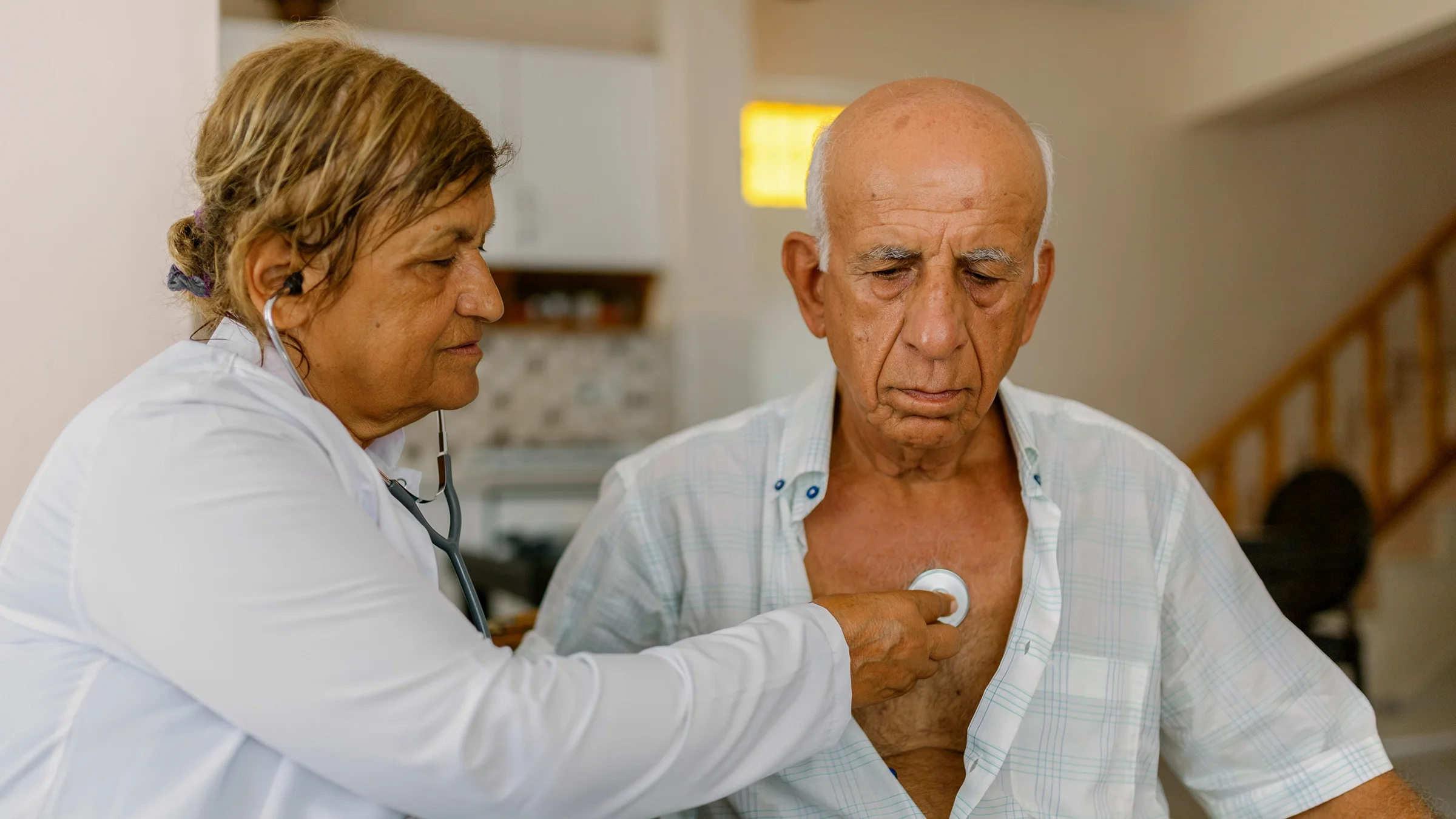 Medical professional listening to older patient's heartbeat.