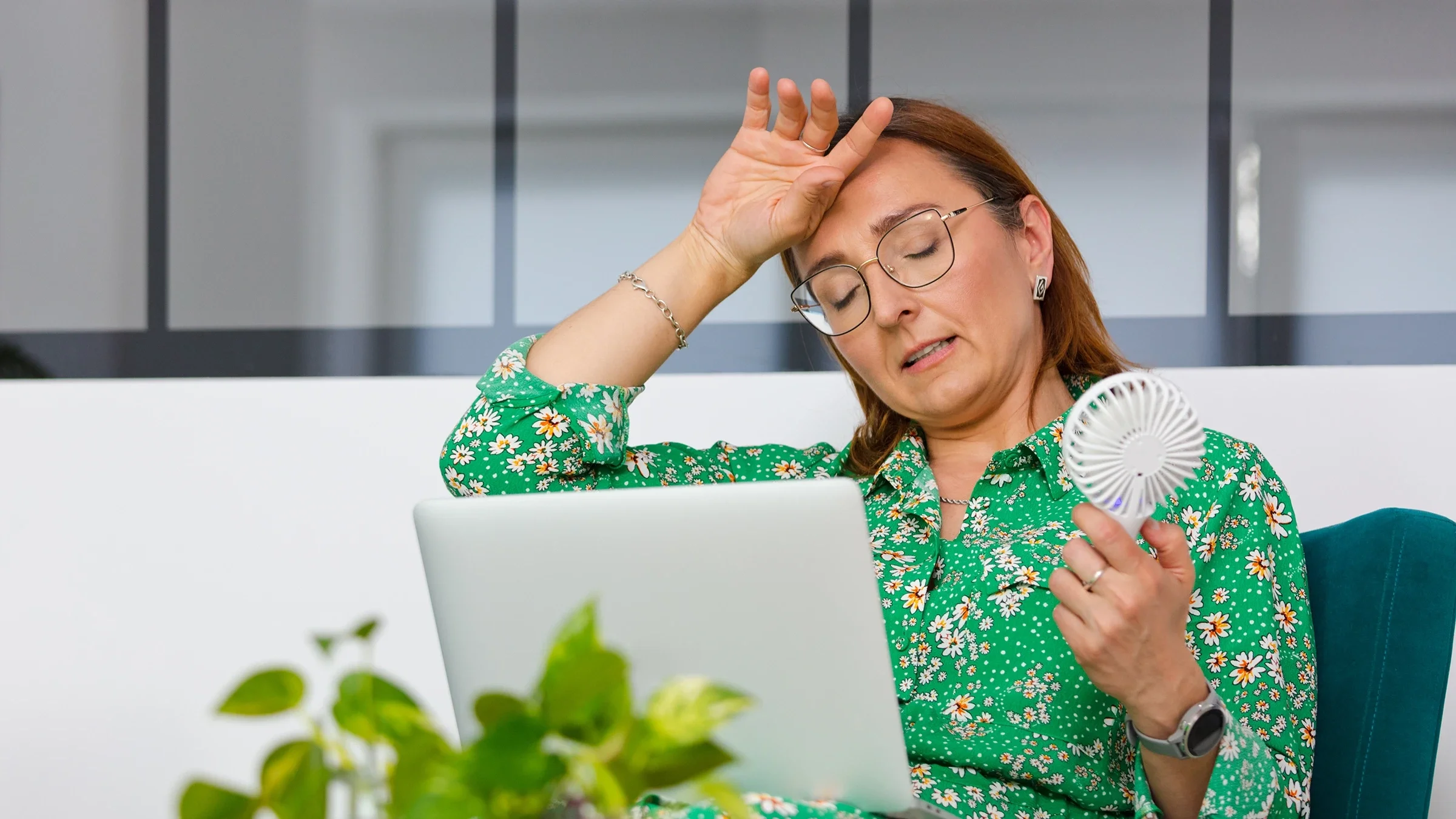 A woman is fanning herself and looking overheated at work.