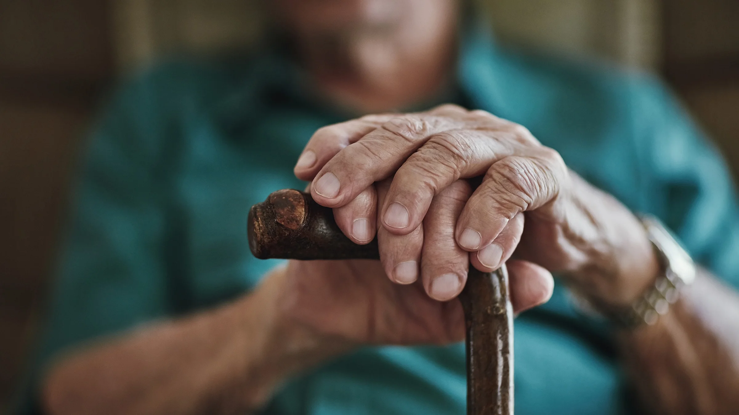 A close-up of a man’s hands resting on a cane.