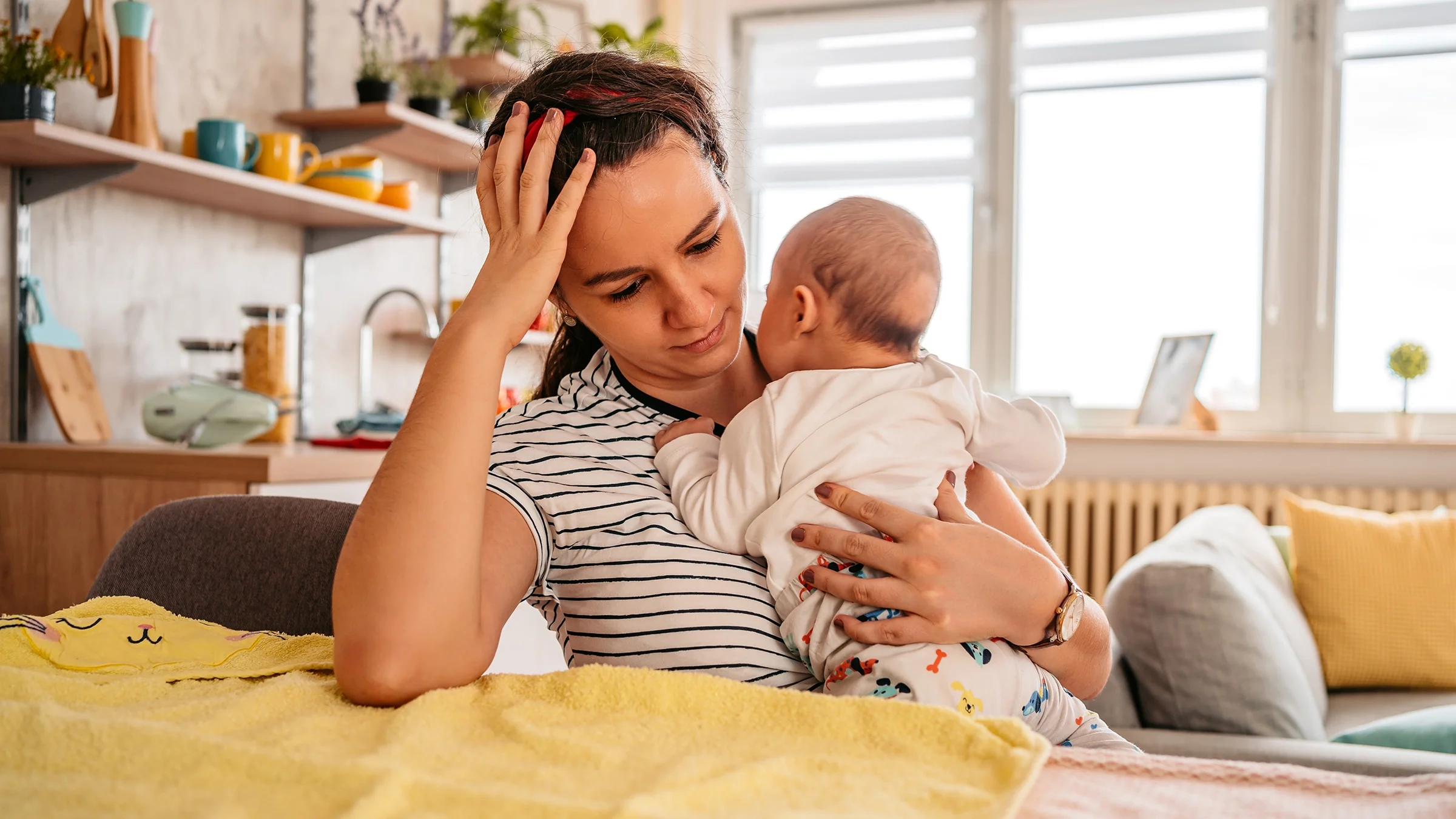 New mother holding her baby while looking sad and experiencing postpartum depression.